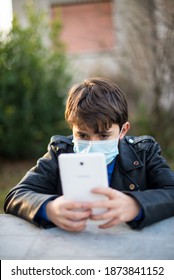 Young Boy With Mask Reads On Tablet, Remote School, Sad Look Sitting In The Garden