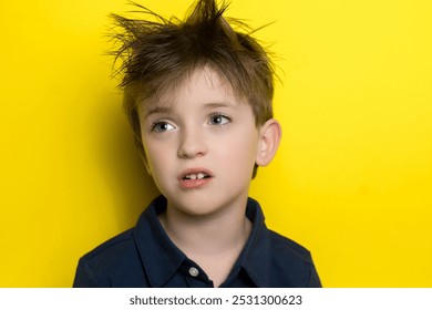 A young boy with messy hair, wearing a navy-blue shirt, looks thoughtfully into the distance against a vibrant yellow background. His casual, curious expression adds a playful touch to the composition - Powered by Shutterstock