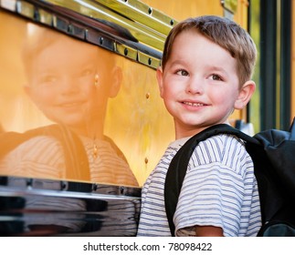 Young Boy With Nervous Smile Waits To Board Bus On First Day Of School.