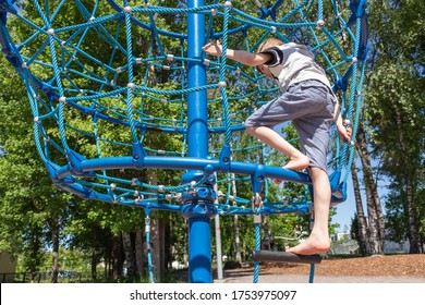 A young boy on the playground barefoot climbs on a rope web. - Powered by Shutterstock