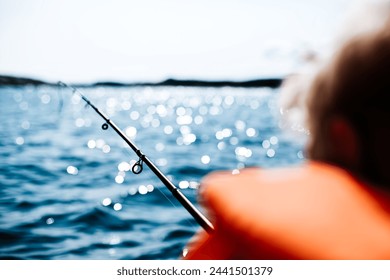 Young boy in orange lifejacket fishing from a boat on a glorious sunny summer day, with sparkling blue sea, in the northern part of Europe.  - Powered by Shutterstock