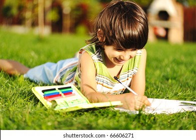 Young Boy Outdoors On The Grass Reading A Book, Writting And Drawing