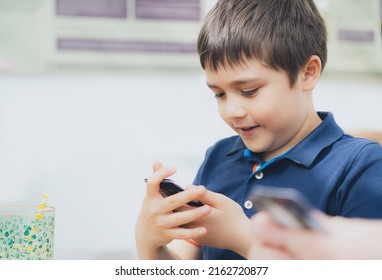 Young Boy Playing Card Game In The Cafe While Waiting For Food, Kid With Curious Face Looking At Paper Card On His Hands,  Family Playing Board Game Indoor On Sunny Day Spring Or Summer.