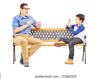 Young Boy Playing Cards With His Older Cousin Seated On Bench Isolated On White Background