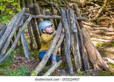 A young boy is playing in the forest in summer or spring. Toddler is building a  wooden hut of logs and branches. Child hiding in wigwam created  in the park. - Powered by Shutterstock