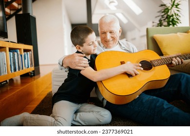 Young boy playing the guitar with his grandfather in the living room - Powered by Shutterstock