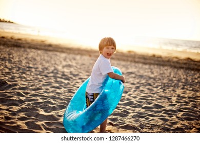 Young boy playing with an inflatable ring, on the sand at the beach.