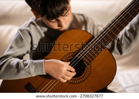 Young boy playing a nylon string acoustic guitar. He is concentrating on learning the instrument, developing musical skills