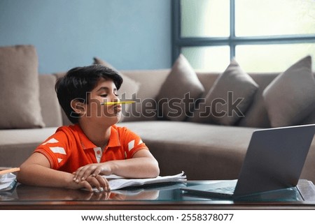 YOUNG BOY PLAYING WITH A PENCIL WHILE ATTENDING A CLASS ONLINE