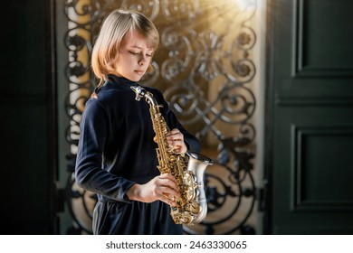 A young boy is playing a saxophone in front of a wrought iron gate. Concept of creativity and passion for music, as the girl is fully engaged in her performance - Powered by Shutterstock