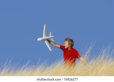 Young Boy Playing With Toy Glider Airplane In Field