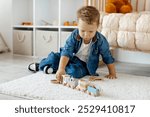 Young boy playing with wooden train set on soft carpet in a cozy indoor play area during daylight hours