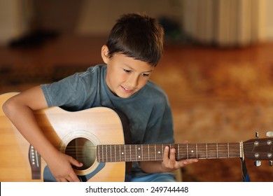 Young boy plays a guitar with very shallow depth of field and warm lighting