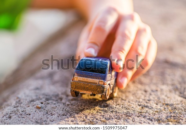 Young boy plays with toy car. Little boy playing\
with car toy on sunset.