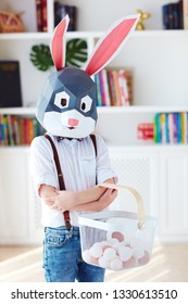 young boy in polygonal easter bunny rabbit mask posing with a basket full of eggs