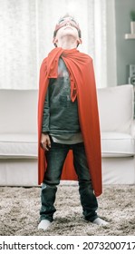 Young Boy Posing In Super Hero Outfit With Red Cape Looking Up At The Sky Indoors In A High Key Living Room At Home