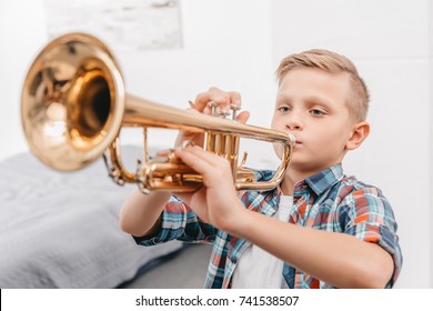 Young boy practicing playing trumpet in living room at home