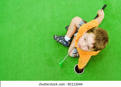 Young boy pulling ball out of hole while playing miniature golf