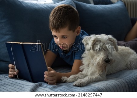 Young boy reading book at home with dog