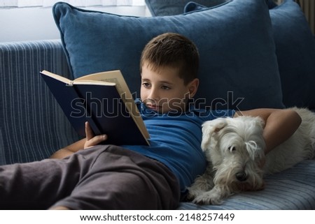 Young boy reading book at home with dog