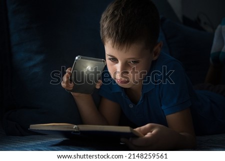 Young boy reading book at night with a lamp from mobile phone