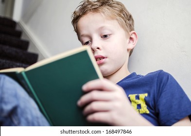 Young boy reading a book on the stairs