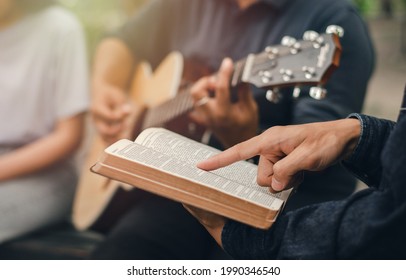 A Young Boy Reads The Bible While His Friend Plays The Guitar. When He Worships God A Small Group Of Christians Or Concepts In A Church At A Church.