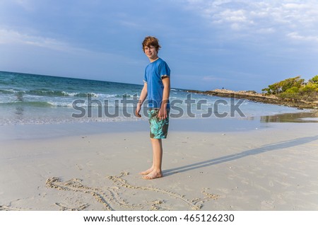 young boy with red hair  is writing a message in the sandy beach