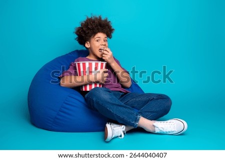 Young boy relaxing on a bean bag chair holding a popcorn bucket against a vibrant blue background
