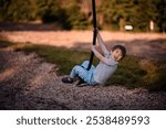 A young boy rides on a zipline in a park, smiling confidently as he enjoys the thrill of the outdoor adventure.