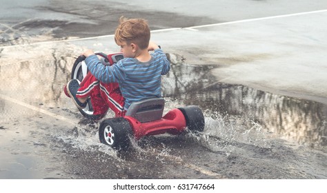 Young Boy Riding A Big Wheel Bike Through A Puddle