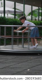 Young boy rotating roundabout while standing upright and gripping steering wheel expressing coordination energy and active engagement within lively playground environment