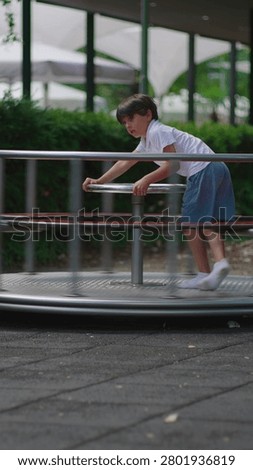 Young boy rotating roundabout while standing upright and gripping steering wheel expressing coordination energy and active engagement within lively playground environment