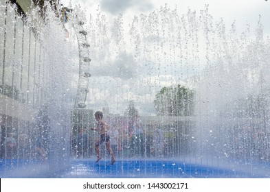 Young Boy Running Inside A Fountain To Cool Down From The Hot Summer Heat, London, England.