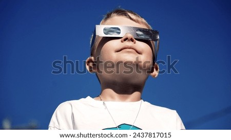 A young boy safely looks at a total eclipse while wearing protective glasses.  	