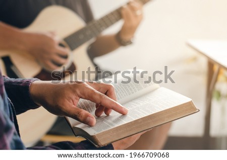 A young boy sat and read the Bible while his friend played guitar at church when he worshiped God. A small group of Christians or a concept in a church at a church