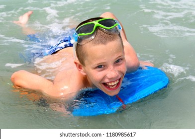 Young Boy Seems To Burst With Glee As He Experiences Boogie Boarding For The First Time.  His Board Is Blue And Has Green Snorkle Glasses.