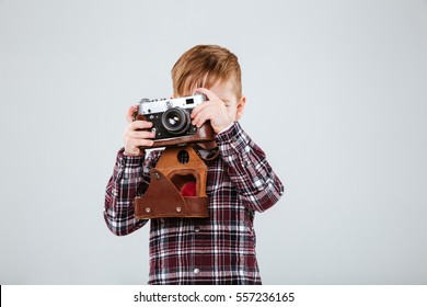 Young Boy In Shirt Making Photo On Retro Camera In Studio. Isolated Gray Background