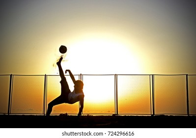 Young boy shooting bicycle kick in front of sunrise in the beach football match