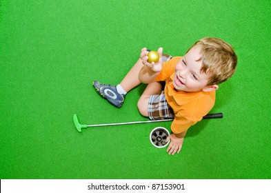 Young boy showing off golf ball after pulling it out of hole while playing miniature golf