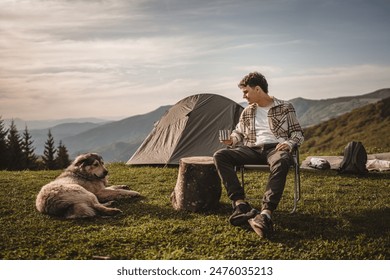 Young boy sit in front tent and drink coffee with dog on the mountain - Powered by Shutterstock