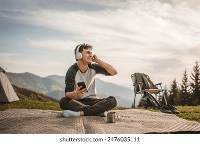 Young boy sit on blanket on the mountain and listen music on headphones and mobile phone - Powered by Shutterstock