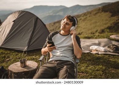 Young boy sit on chair on the mountain listen music on headphones and mobile phone - Powered by Shutterstock