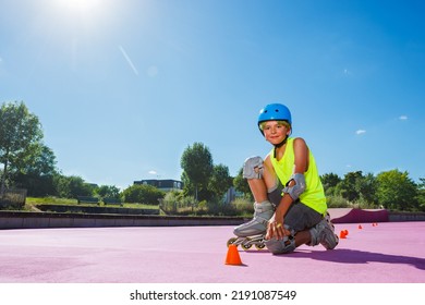 Young Boy Sit And Pose In Blue Helmet With Rollerblades In The Skatepark Wearing Protection