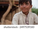 A young boy sits in a refugee camp, wearing a white shirt and looking thoughtful.