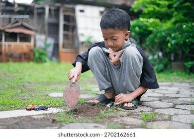 A young boy sits in the yard while digging soil using a small gardening shovel, playing with toy cars on the ground. The scene captures a candid outdoor moment of childhood play and creativity.	