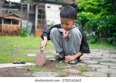A young boy sits in the yard while digging soil using a small gardening shovel, playing with toy cars on the ground. The scene captures a candid outdoor moment of childhood play and creativity.	