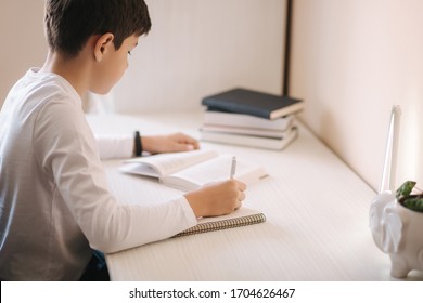 Young boy sitting at desk read the book and write down in notebook. Study at home during quarantine
