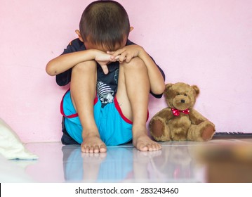 Young boy, sitting on the floor, teddy bear next to him, crying, looking away