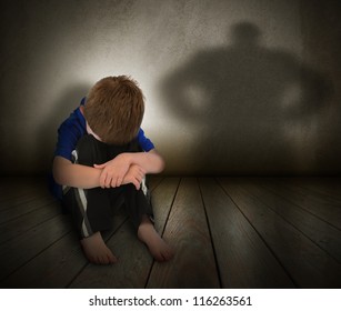 A young boy is sitting on the ground and scared with his face covered. There is a shadow silhouette on the wall to represent abuse, fear,  or a bully.